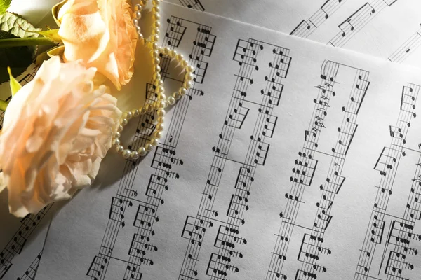 Beautiful roses with pearls on music sheets background — Stock Photo, Image
