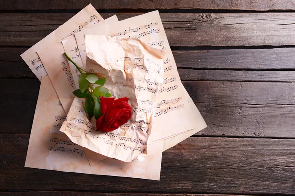 Mooie roos op verfrommeld muziek bladen op houten achtergrond — Stockfoto