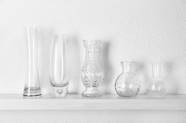 Decorative glass vases on wooden shelf on white wallpaper background