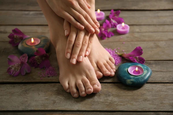 Vrouwelijke voeten bij spa pedicure procedure met bloemen en kaarslicht op houten achtergrond — Stockfoto