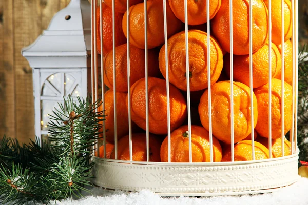 Mandarijnen in decoratieve kooi met kerst decor, op houten achtergrond — Stockfoto