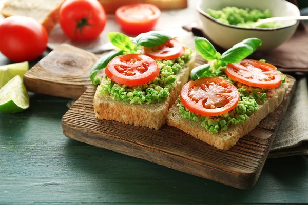 Vegan sandwich with avocado and vegetables on cutting board, on wooden background — Stock Photo, Image