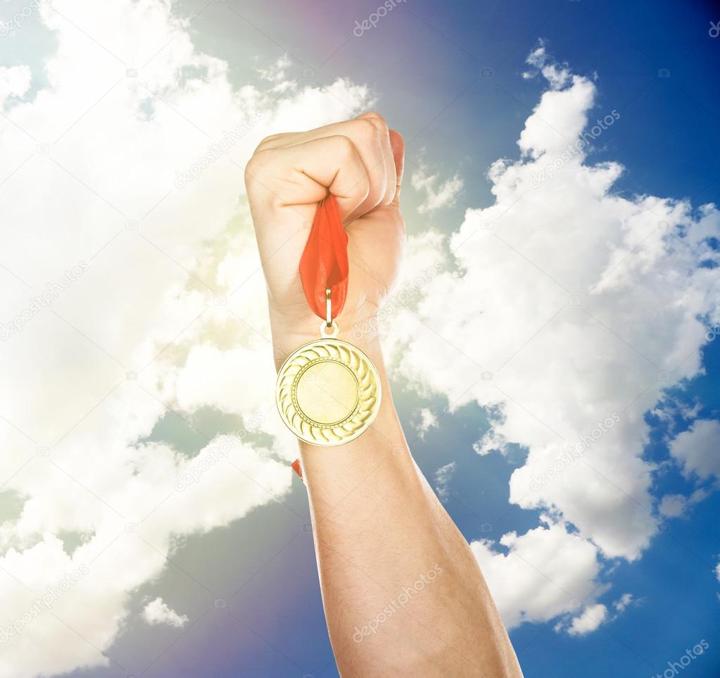 Golden medal in hand on sky background