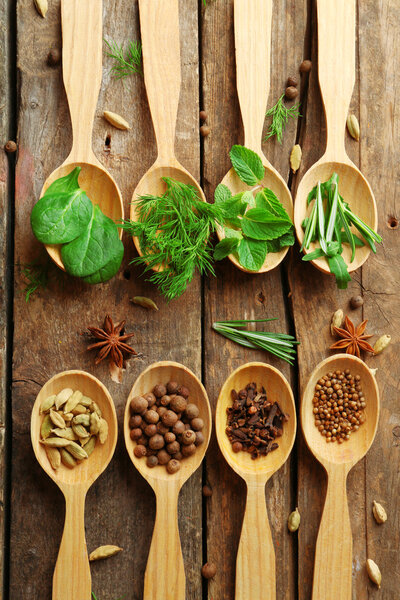 Wooden spoons with fresh herbs and spices on wooden background