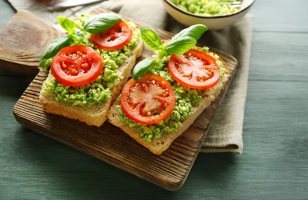Sandwich vegano con aguacate y verduras sobre tabla de cortar, sobre fondo de madera — Foto de Stock