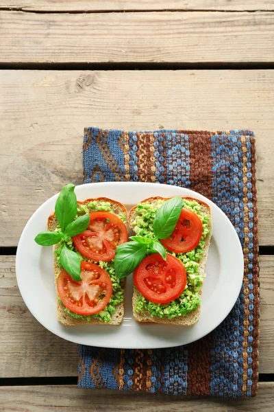 Panino vegano con avocado e verdure su piatto, su fondo di legno — Foto Stock