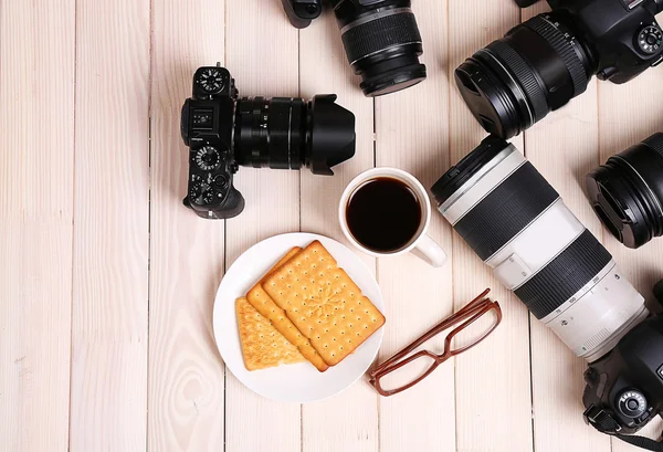 Moderna kameror med glasögon, kopp kaffe och kakor på träbord, ovanifrån — Stockfoto