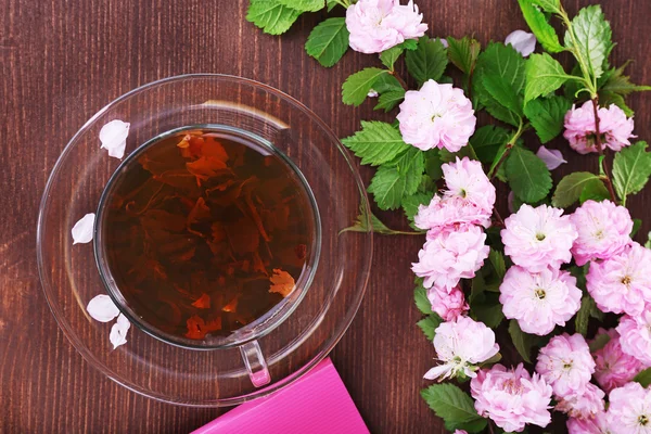 Xícara de chá de ervas com rosas cor-de-rosa na mesa de madeira, vista superior — Fotografia de Stock