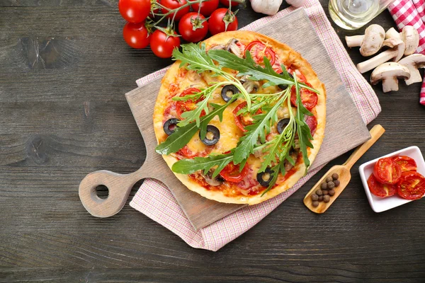 Tasty pizza with vegetables and arugula on cutting board on table close up — Stock Photo, Image