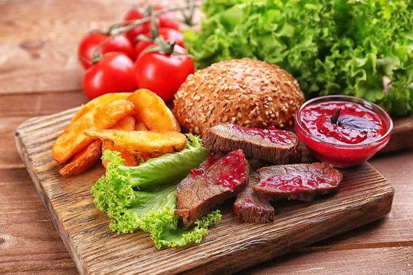 Carne com molho de cranberry, fatias de batata assada e pão na tábua de corte, no fundo de madeira — Fotografia de Stock