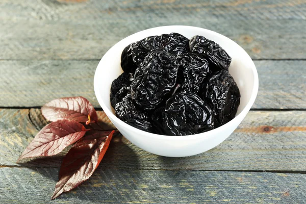 Saucer of prunes with leaves on wooden table, closeup — Stock Photo, Image