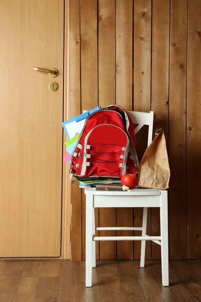 Batoh s školní potřeby na židli na dřevěné pozadí — Stock fotografie