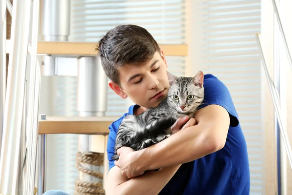 Jovem bonito com gato bonito sentado em passos em casa — Fotografia de Stock