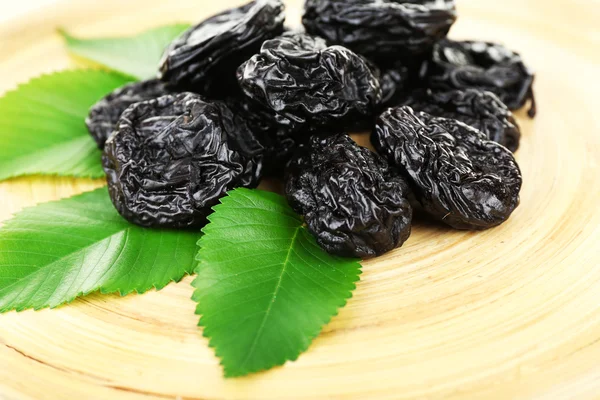 Pile of prunes with leaves on wooden tray, closeup — Stock Photo, Image