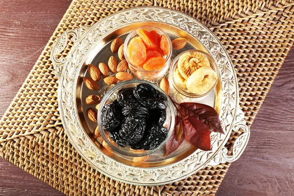 Śliwki i innych suszonych owoców w szklanych talerzy z winogron pozostawia na metalowej tacy i maty wiklinowe, widok z góry — Zdjęcie stockowe