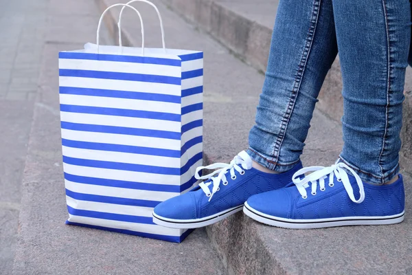 Female feet in gumshoes near shopping bag on  stone stairs — Stock Photo, Image