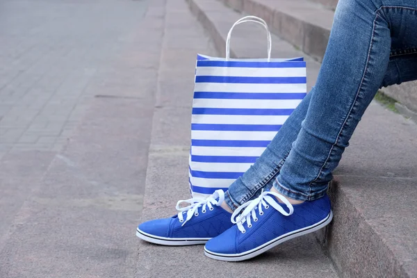 Female feet in gumshoes near shopping bag on  stone stairs — Stock Photo, Image