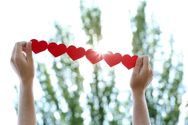 Manos femeninas con cadena de corazones de papel sobre fondo natural —  Fotos de Stock