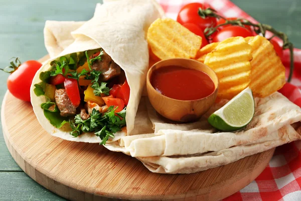 Burrito fatto in casa gustoso con verdure, patatine sul tagliere, su sfondo di legno — Foto Stock