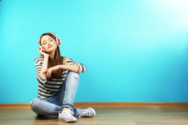 Young woman sitting on floor with headphones on turquoise wallpaper background — Stock Photo, Image