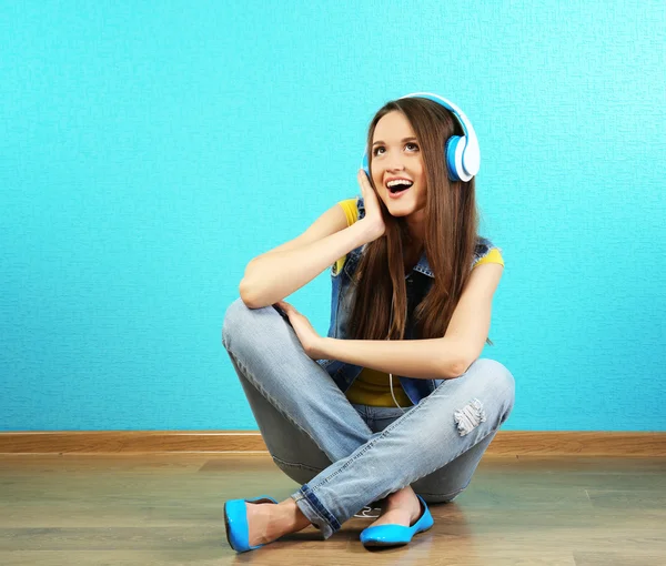 Young woman sitting on floor with headphones on turquoise wallpaper background — Stock Photo, Image