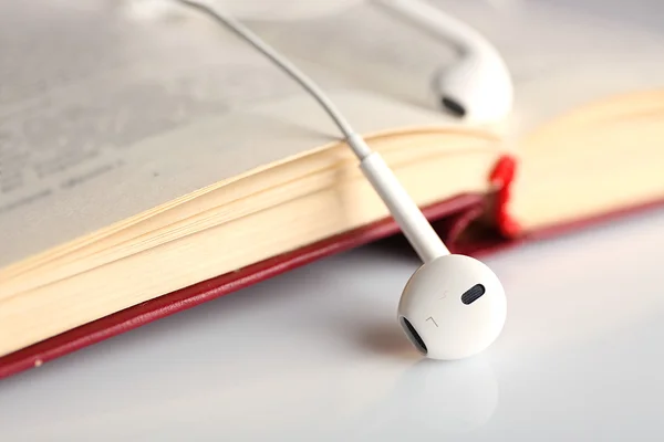 Oortelefoons en boek op tafel, close-up — Stockfoto