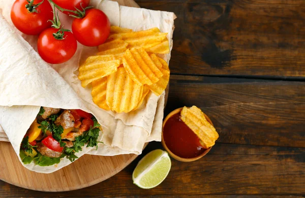 Домашнее вкусное буррито с овощами и картофельными чипсами на доске, на деревянном фоне — стоковое фото