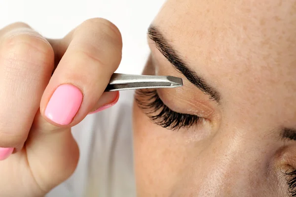 Jonge vrouw plukken wenkbrauwen met pincet sluiten — Stockfoto