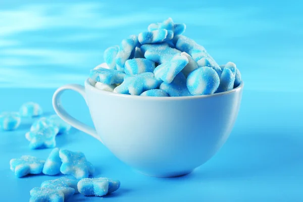 Süße Bonbons in Tasse auf hellblauem Hintergrund — Stockfoto