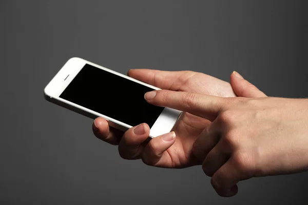Manos sosteniendo el teléfono inteligente móvil sobre fondo gris — Foto de Stock