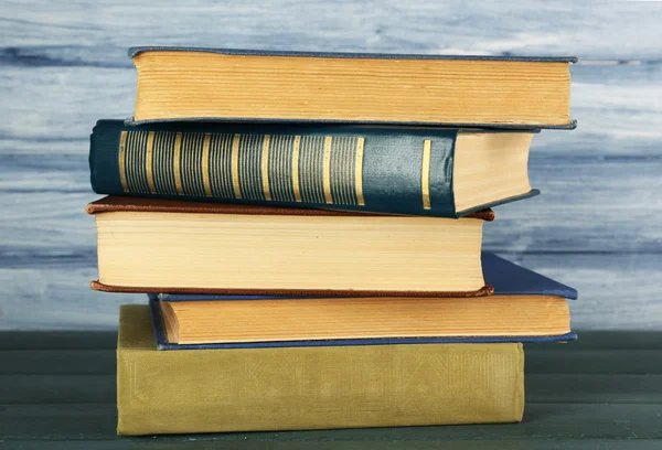 Montón de libros sobre mesa de madera sobre fondo de pared de madera azul — Foto de Stock