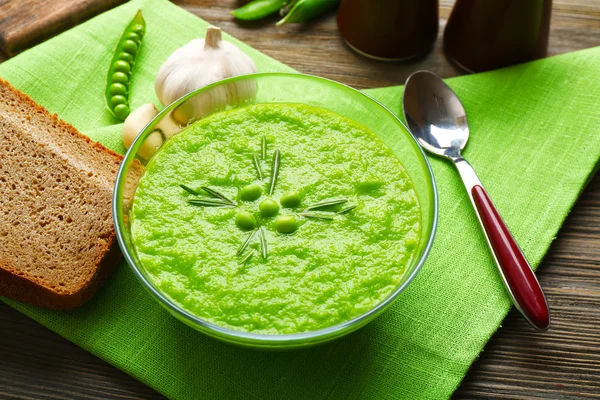 Green pea soup in glass bowl on wooden table with napkin, closeup — Stock Photo, Image