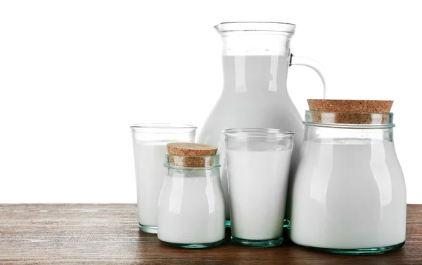 Pitcher, jars and glasses of milk on wooden table, on white background — Stock Photo, Image