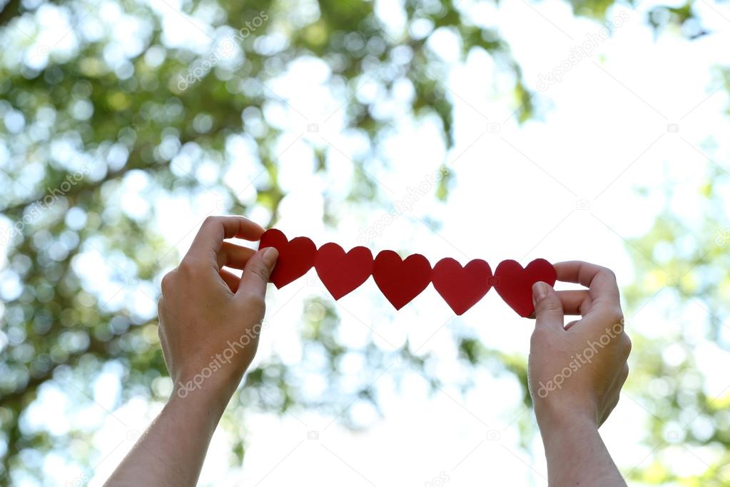 Female hands with chain of paper hearts over nature background