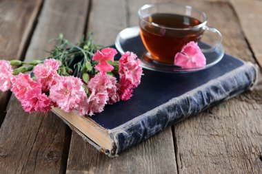 Ahşap masa üzerine güzel çiçekler ve çay ile eski kitap yakın çekim