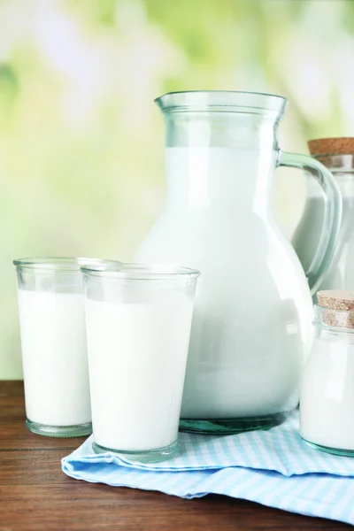 Jarra, frascos y vasos de leche sobre mesa de madera, sobre fondo natural —  Fotos de Stock