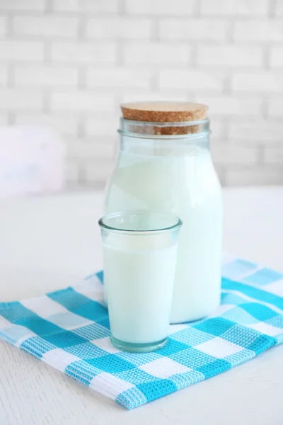 Kruik en glas melk op houten tafel, op bakstenen muur achtergrond — Stockfoto