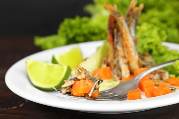 Fried small fish with carrot and greens on table close up — Stock Photo, Image