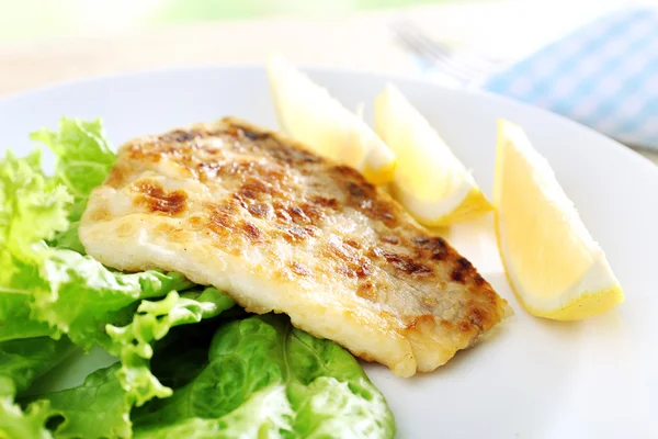 Dish of fish fillet with lettuce and lemon on table close up — Stock Photo, Image