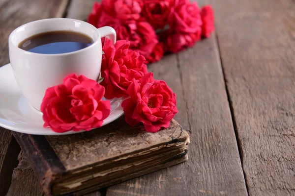 Gammal bok med vackra rosor och kopp kaffe på träbord nära håll — Stok fotoğraf