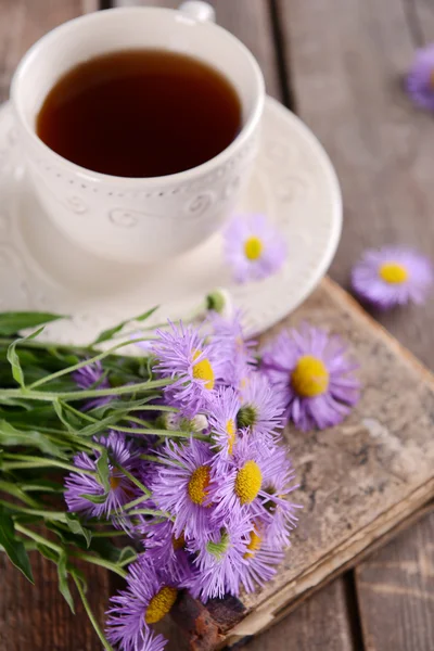 Old book with beautiful flowers and cup of tea on wooden table close up — Stock Photo, Image