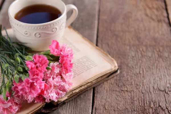 Old book with beautiful flowers and cup of tea on wooden table close up — Stock Photo, Image