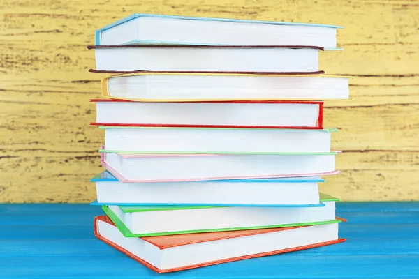 Empilhar livros sobre fundo de madeira amarelo — Fotografia de Stock