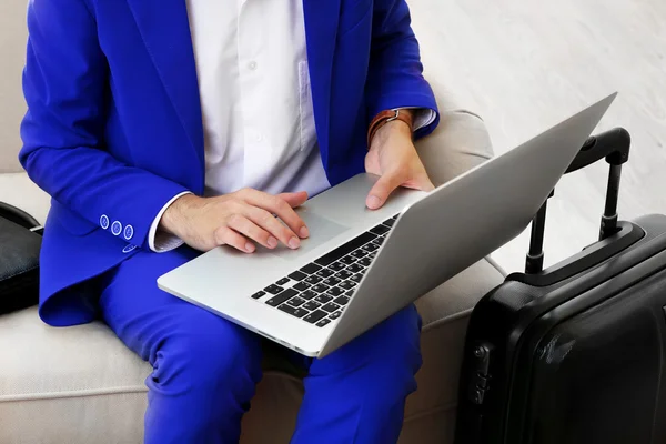 Business man with suitcase and laptop sitting on sofa in hall — Stock Photo, Image