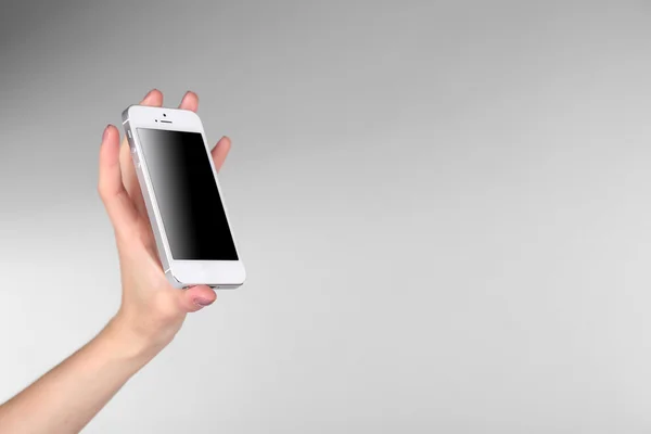 Ręka trzyma telefon inteligentny na szarym tle — Zdjęcie stockowe