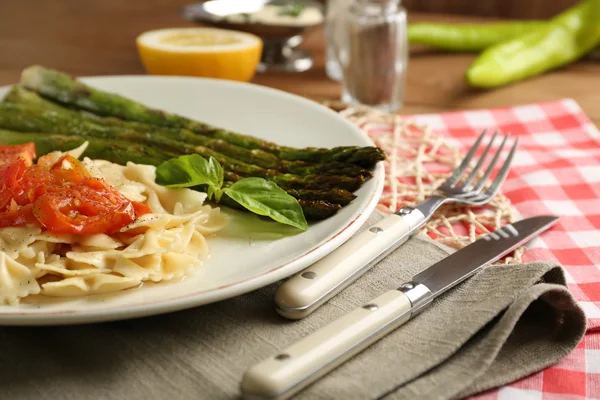 Жареная спаржа и вкусная паста с овощами на тарелке на фоне деревянного стола — стоковое фото