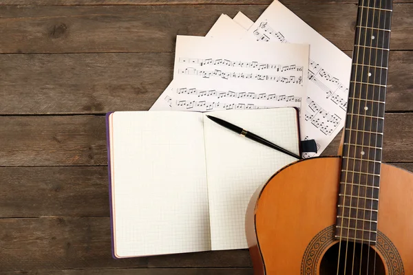 Cena de gravação musical com violão, caderno e folhas de música em mesa de madeira, close-up — Fotografia de Stock