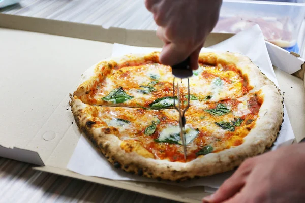 Macho mão corte pizza com lâmina de pizza na caixa, close-up — Fotografia de Stock