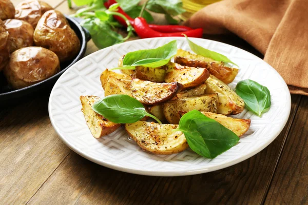 Gebakken aardappelen met basilicum in witte plaat op houten tafel, close-up — Stockfoto