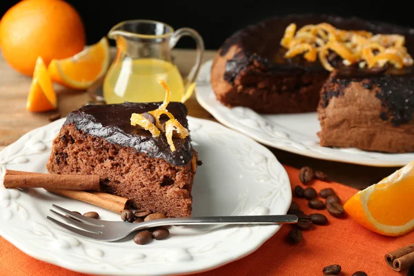 Kage med chokoladeglasur og orange på plade, på træbaggrund - Stock-foto